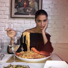 a woman sitting at a table in front of a plate of spaghetti with lobsters