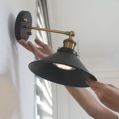 a person is holding the arm of a wall light in their right hand and reaching for it