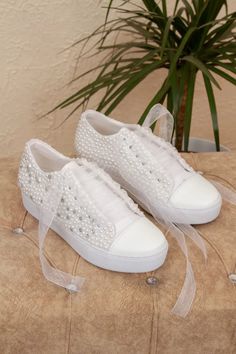 a pair of white shoes with pearls on them sitting next to a potted plant