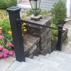 a street light sitting on top of a stone block wall next to flowers and bushes