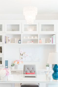 a white desk topped with a laptop computer next to a lamp and bookshelf