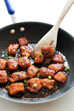 a pan filled with meat and sauce on top of a table next to a wooden spoon