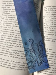 an octopus bookmark sitting on top of an open book with watercolors and ink