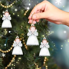 a hand is holding an ornament on a christmas tree with three angels hanging from it