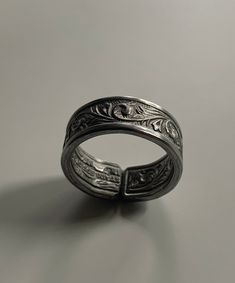 a silver ring with intricate designs on the outside and inside, sitting on a gray surface