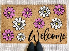 someone standing in front of a welcome mat with pink and white daisies on it