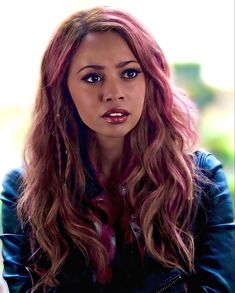 a woman with long red hair wearing a black leather jacket and looking at the camera