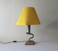 a lamp that is on top of a wooden base and has a yellow shade over it