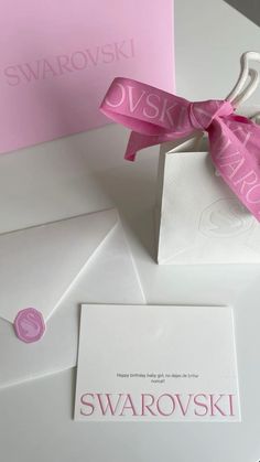 the pink ribbon is tied on top of the white envelope and it says swaroskii