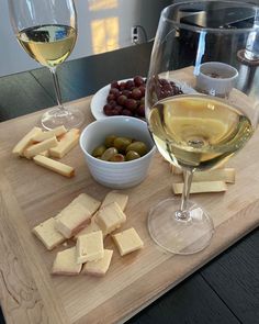 two glasses of wine, cheese and olives on a cutting board