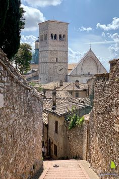 an alley way with stone buildings and cobblestone walkway leading up to the bell tower