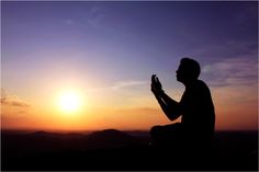 a man sitting on top of a hill praying