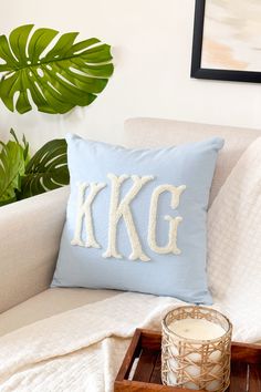 a blue pillow sitting on top of a white couch next to a wooden tray with a candle