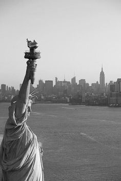 black and white photograph of the statue of liberty in new york city, with manhattan behind it