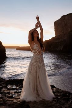 a woman standing on top of a beach next to the ocean wearing a wedding dress