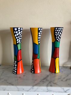 three colorful vases sitting on top of a marble counter