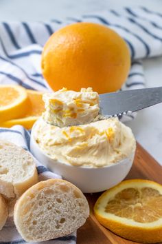 a knife is sticking into a bowl of whipped cream next to sliced oranges and bread on a cutting board