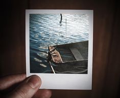 a person holding up a polaroid photo of a boat in the water with one hand