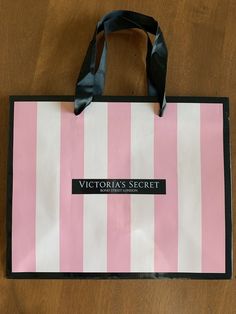 a pink and white striped shopping bag sitting on top of a wooden table next to a black ribbon