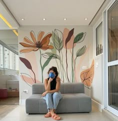 a woman sitting on a couch in front of a wall with flowers painted on it