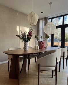 a dining room table with chairs and vases on it's centerpiece in front of a large window