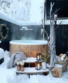 a hot tub surrounded by snow covered trees and other outdoor furniture, with candles on the table