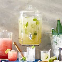 a table topped with glasses and pitchers filled with drinks next to ice buckets full of lemonade