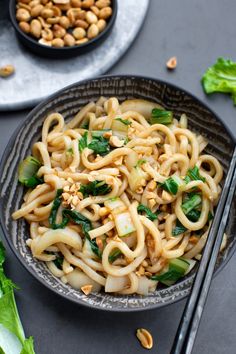 a bowl filled with noodles and vegetables next to chopsticks on a table top