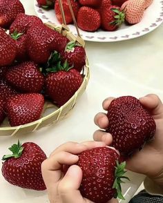 a person is picking strawberries from a basket on a table with other plates and bowls