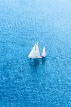 a small white boat floating on top of a large blue body of water with two sails