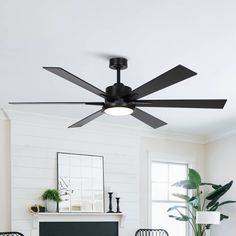 a ceiling fan in a living room with white walls and black chairs around the fireplace