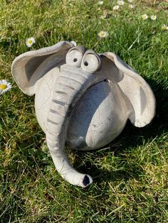 an elephant statue laying in the grass with its trunk sticking out and eyes wide open