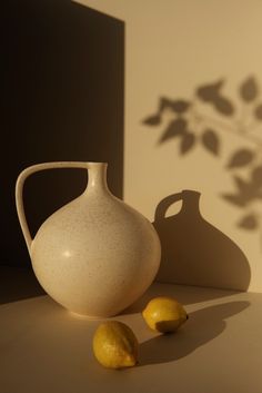 a white vase sitting on top of a table next to two lemons