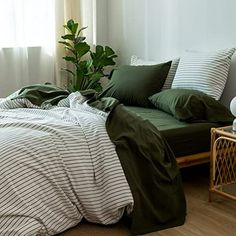 a bed with green sheets and pillows in a room next to a window, near a plant