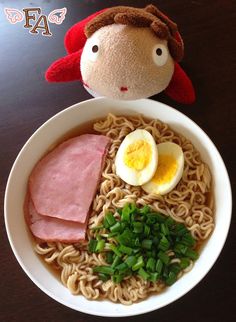 a bowl of ramen with an egg, ham and green onions in it next to a stuffed animal