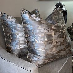 two silver pillows sitting on top of a gray couch