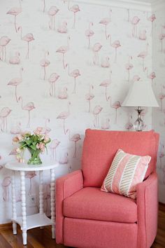 a pink chair sitting next to a white table with a vase on top of it