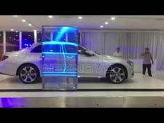 a man standing next to a white car in a showroom with people looking at it