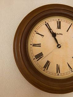 an old clock hanging on the wall with roman numerals and brown wood frame