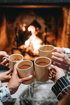 four people holding coffee mugs in front of a fire place with their hands together