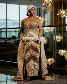 a woman standing in front of a glass wall wearing a gold and white dress with feathers on it