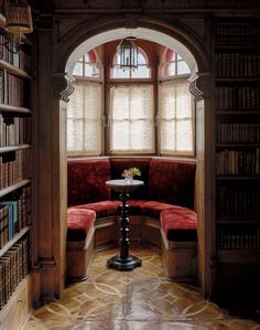 a corner table in the middle of a room with bookshelves and a round window