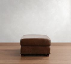 a brown foot stool sitting on top of a wooden floor next to a white wall