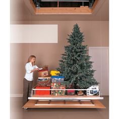 a woman standing in front of a christmas tree with presents on the shelf below it