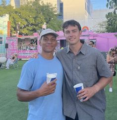 two men standing next to each other holding cups in front of a pink and white tent