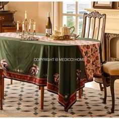 a dining room table covered with a green tablecloth and two chairs in front of a fireplace