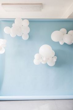 white balloons are floating in the air above a blue wall with clouds painted on it