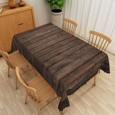 a dining room table with chairs and a brown tablecloth on it, in front of a window