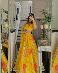 a woman taking a selfie while wearing a yellow floral print lehenga and matching crop top