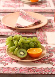 a plate with grapes, oranges and kiwi on it sitting on a table